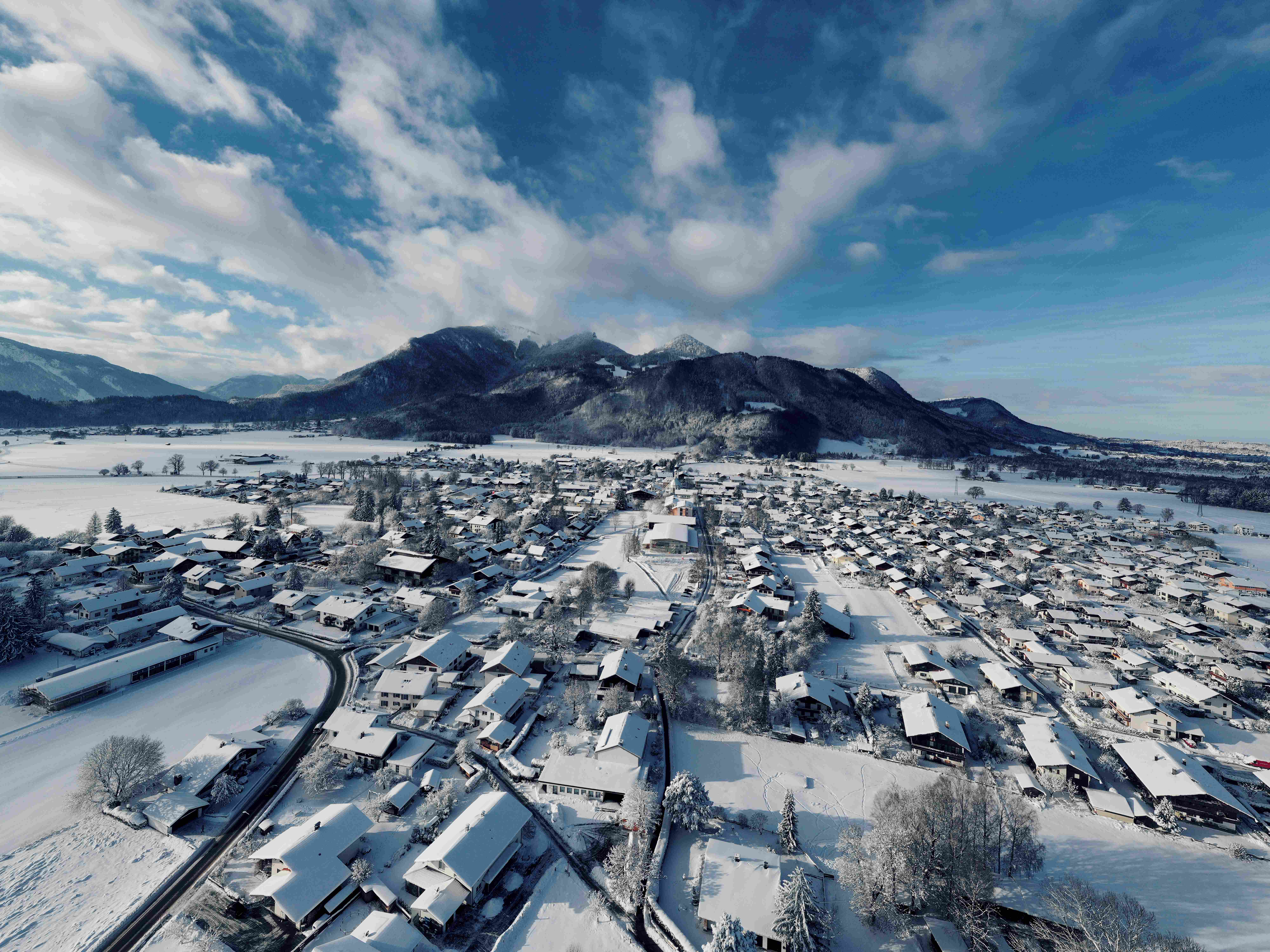 Luftaufnahme eines verschneiten Dorfes mit Bergpanorama