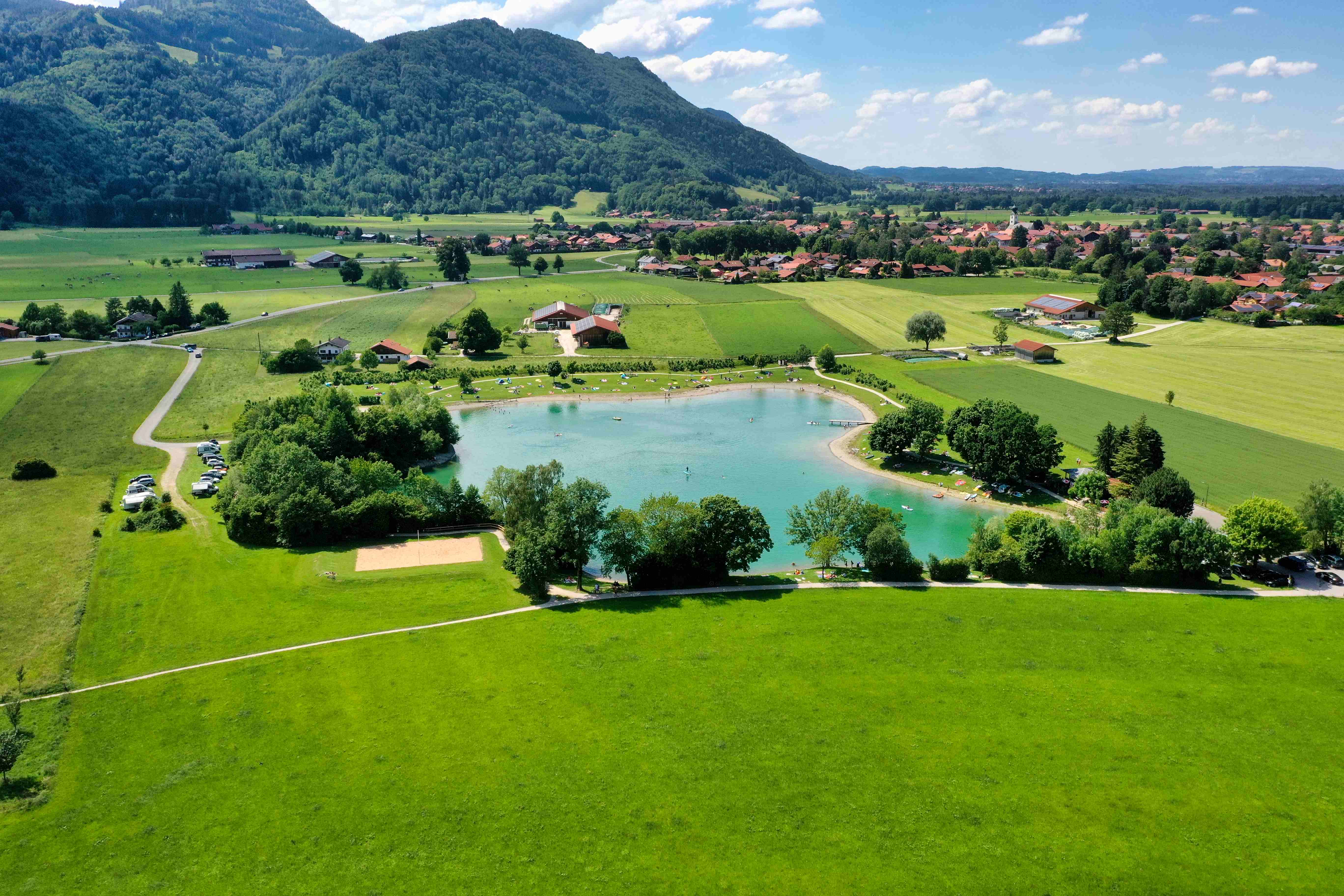 Badesee mit türkisem Wasser umgeben von Wiesen und Bergen